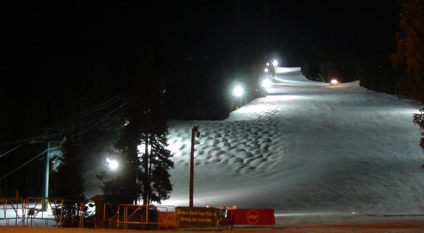 A floodlit ski run at night with the lift gate and pass scanner at the bottom