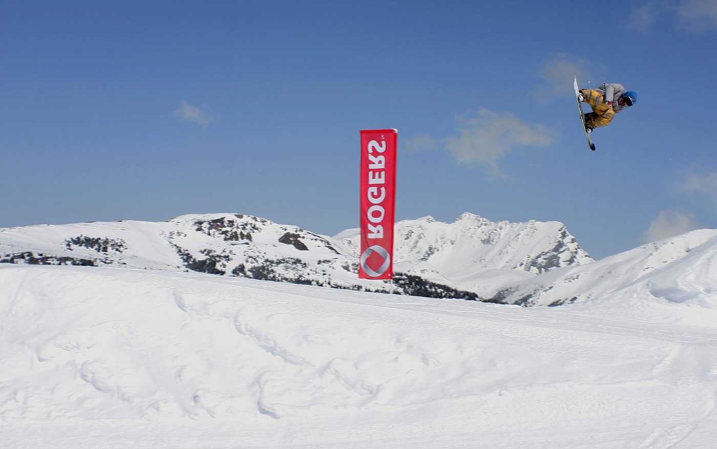 A snowboarder grabbing mid-air over a big jump at Banff Sunshine, with mountains behind