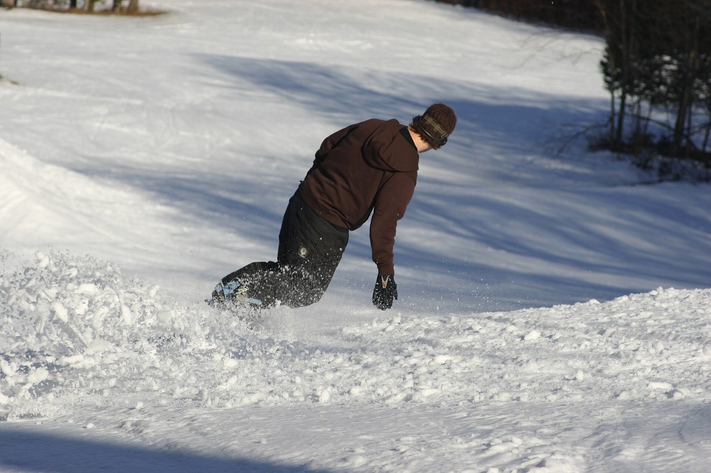 A snowboarder carving a heel-side turn on a groomed slope, the goal of snowboarding for beginners