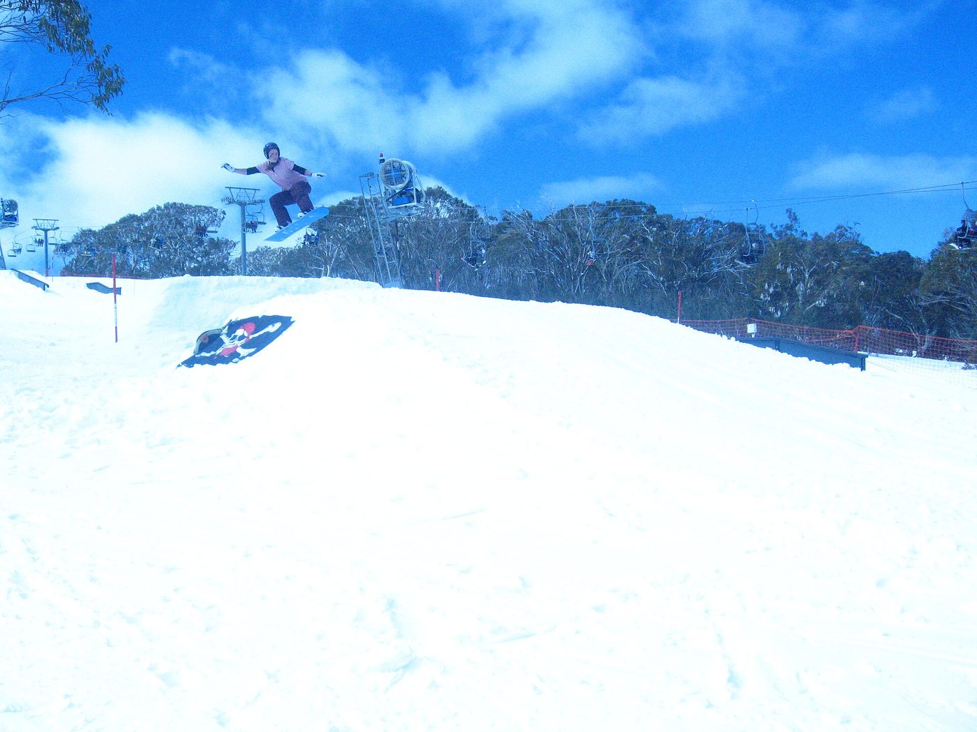 A snowboarder airing a small jump in a beginner-friendly terrain park at Selwyn Snowfields, Australia