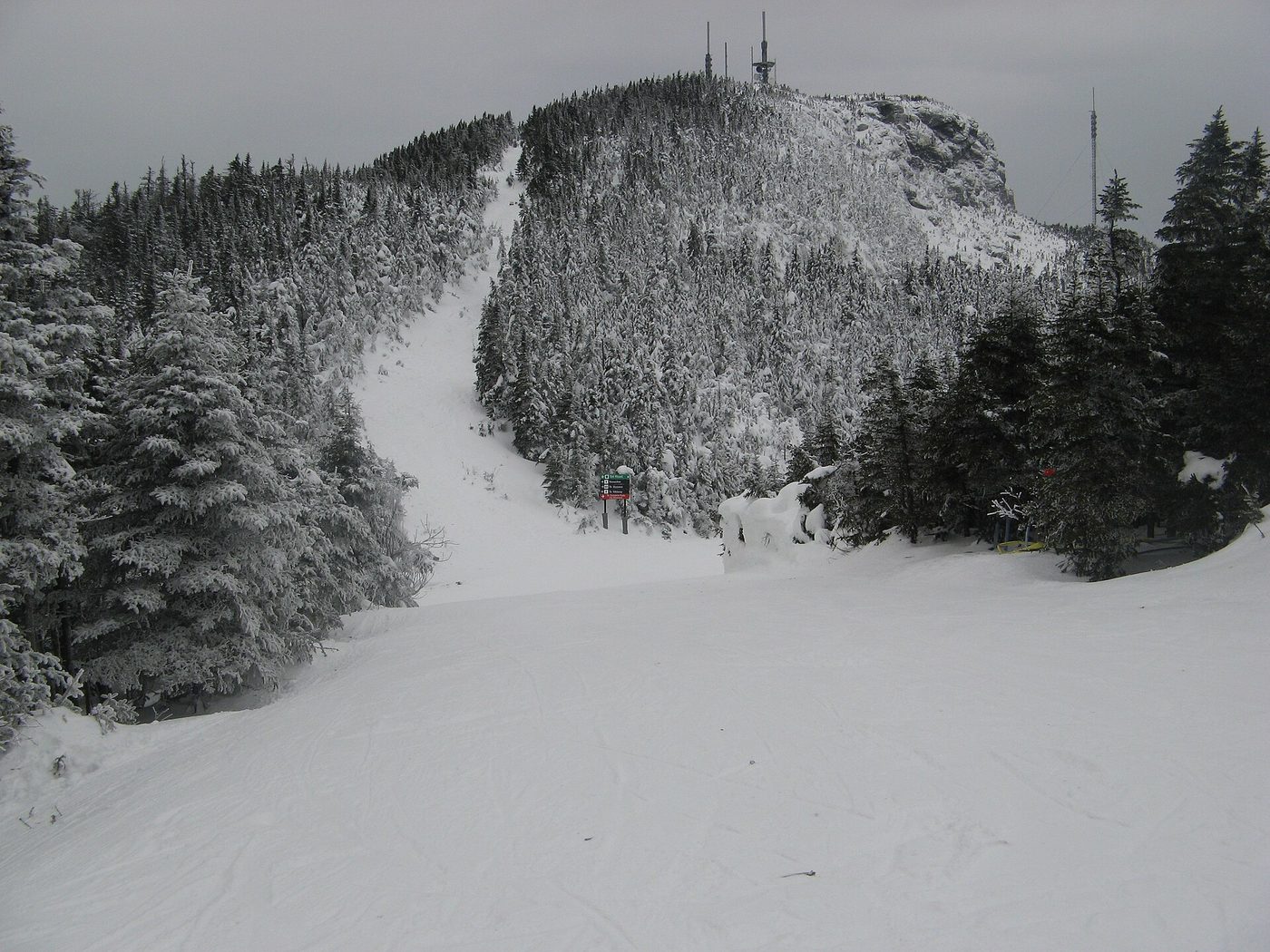 A ski trail dropping through snow-covered evergreens toward the rocky summit of Mt. Mansfield at Stowe, Vermont
