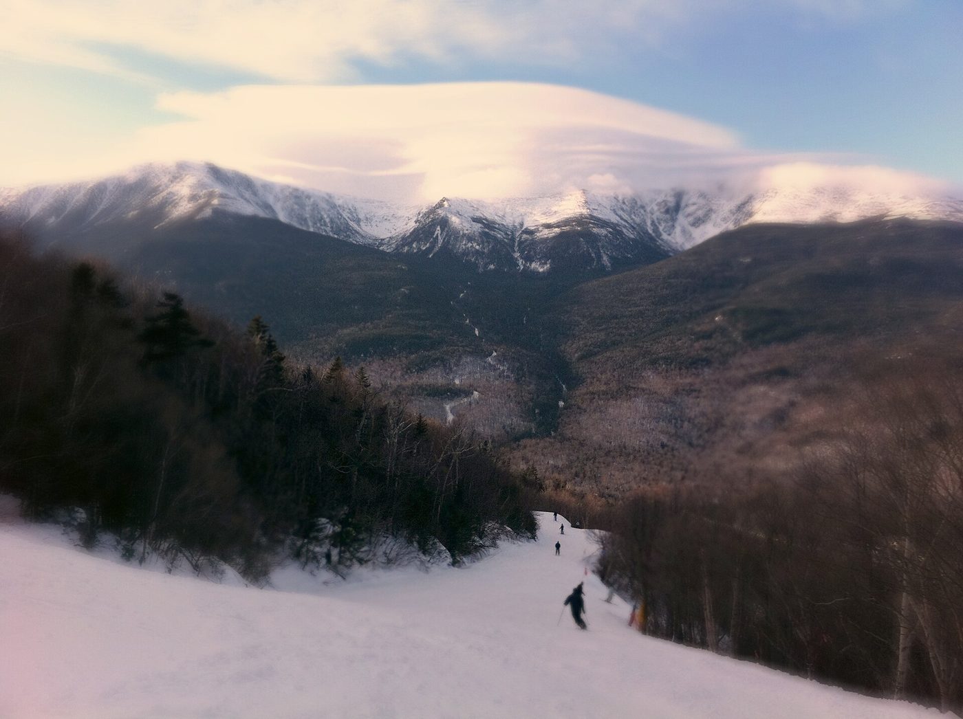 Skiers descending a trail at Wildcat Mountain, New Hampshire, looking across Pinkham Notch toward Mount Washington